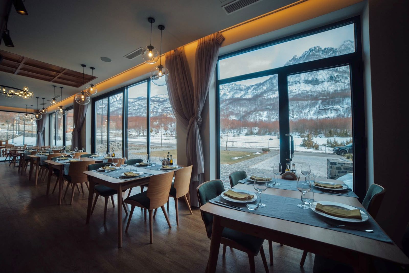Un restaurante con mesas dispuestas para comer, amplias ventanas con vistas a montañas nevadas.