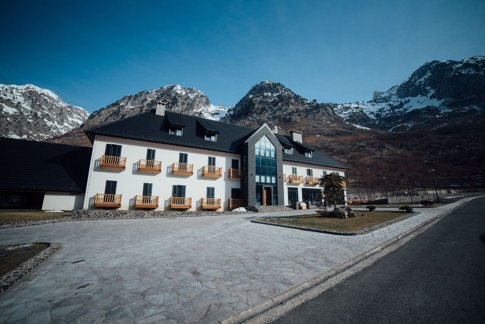 Un hotel con fachada blanca, varios balcones y un acceso empedrado.