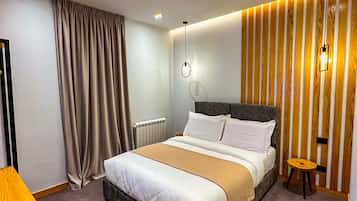 Habitación de hotel moderna con una cama grande, una mesita de noche, un taburete pequeño y una lámpara fijada a la pared.