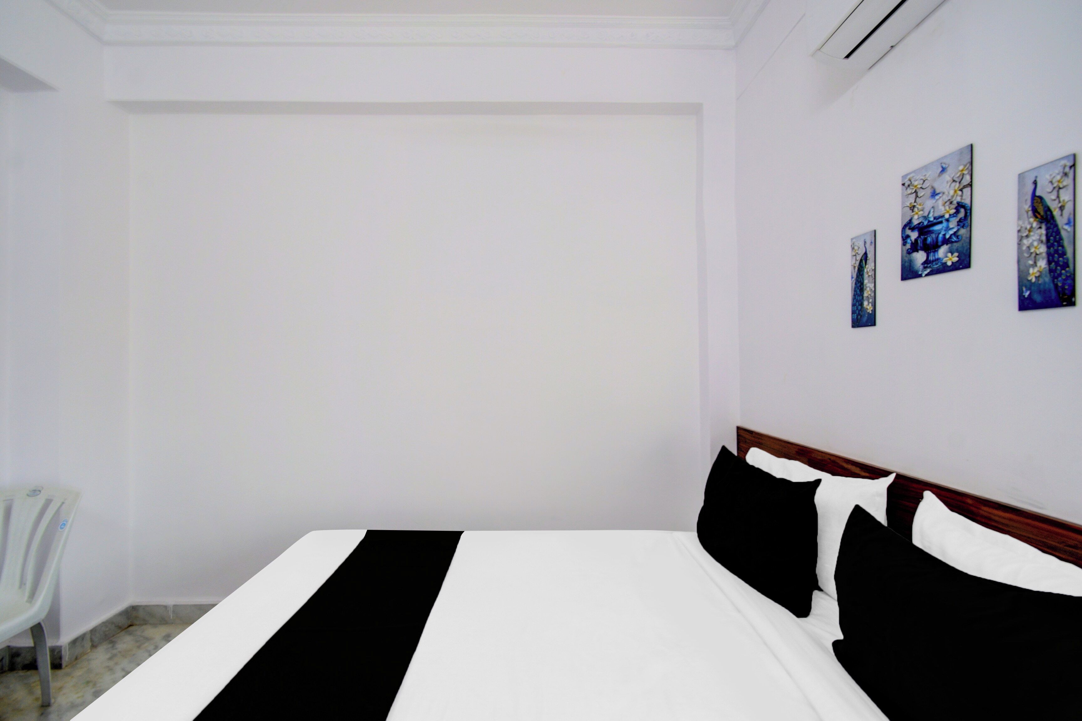 A bedroom with a bed, a chair, and three wall-mounted paintings.