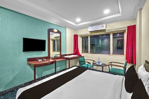 Una habitación de hotel con cama, escritorio, silla, televisor y ventana con cortinas.