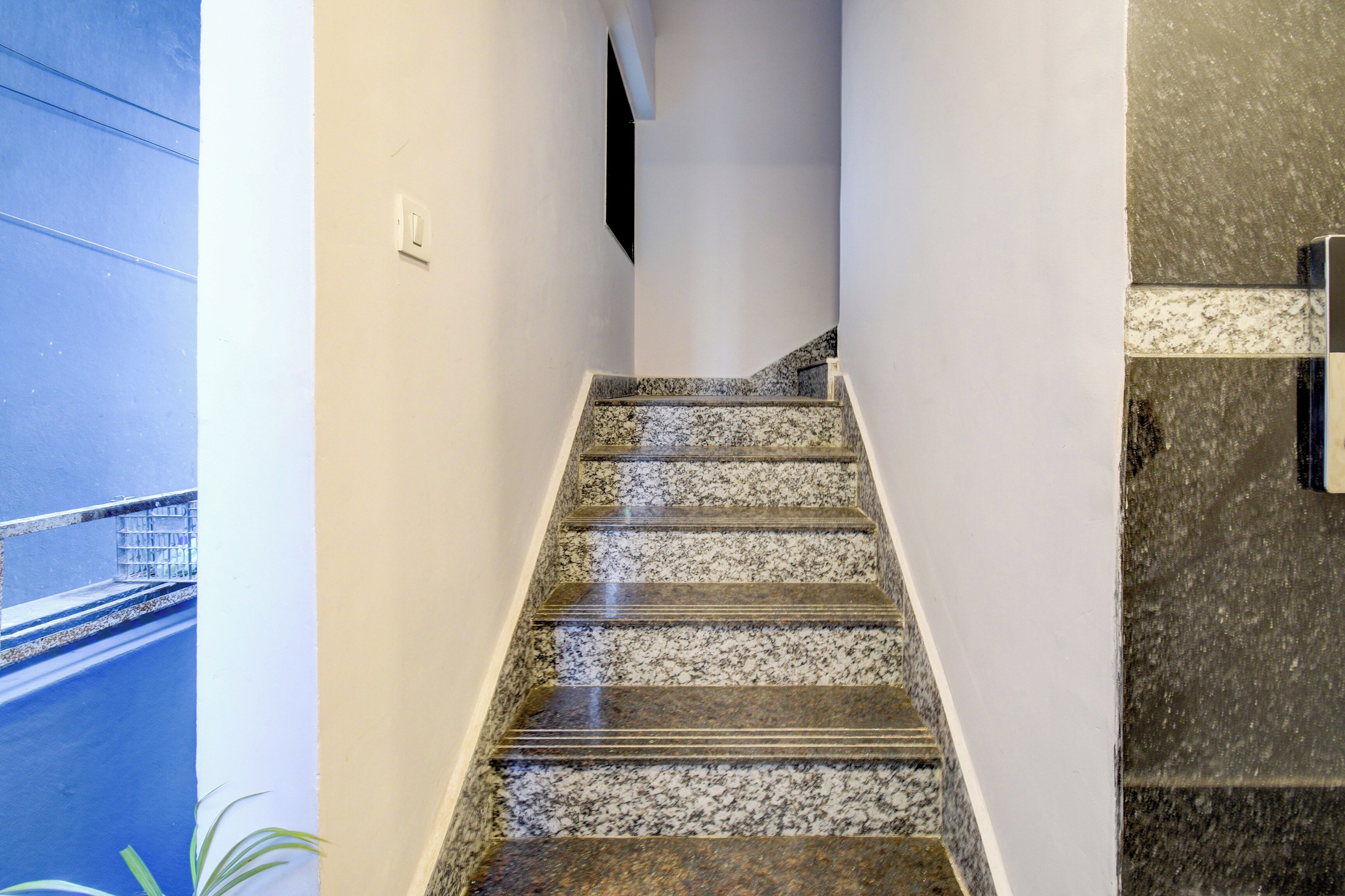 A staircase with a granite finish, leading to a landing with a white wall and a light switch.