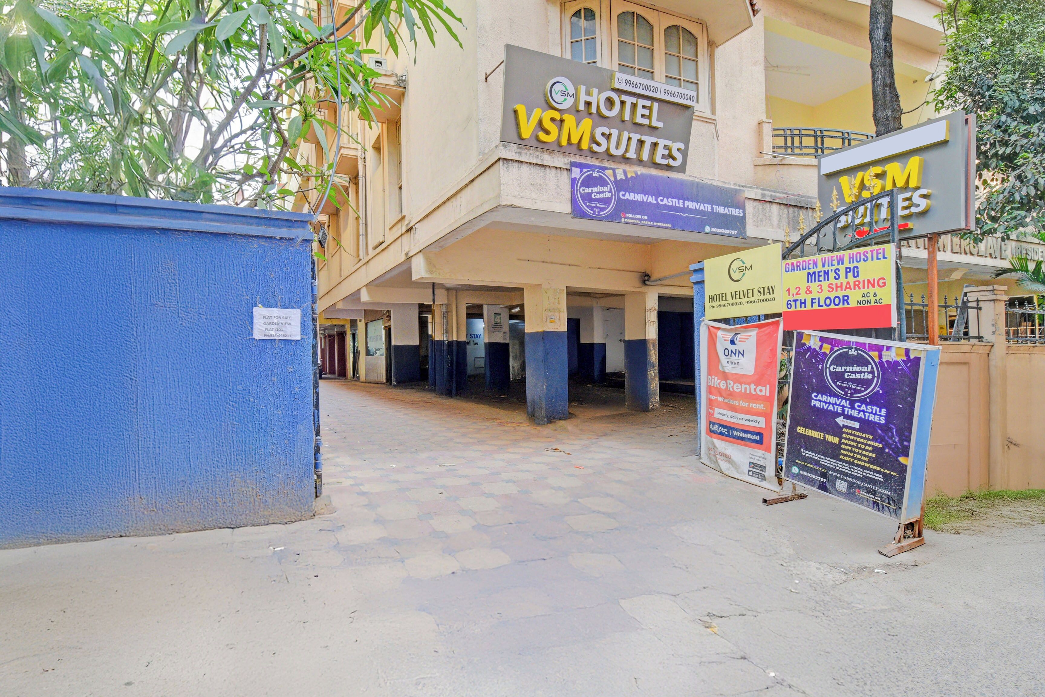 L’entrée d’un hôtel, avec une enseigne indiquant « VSM Suites », un appartement à vendre et diverses publicités, notamment pour un service de location de vélos.