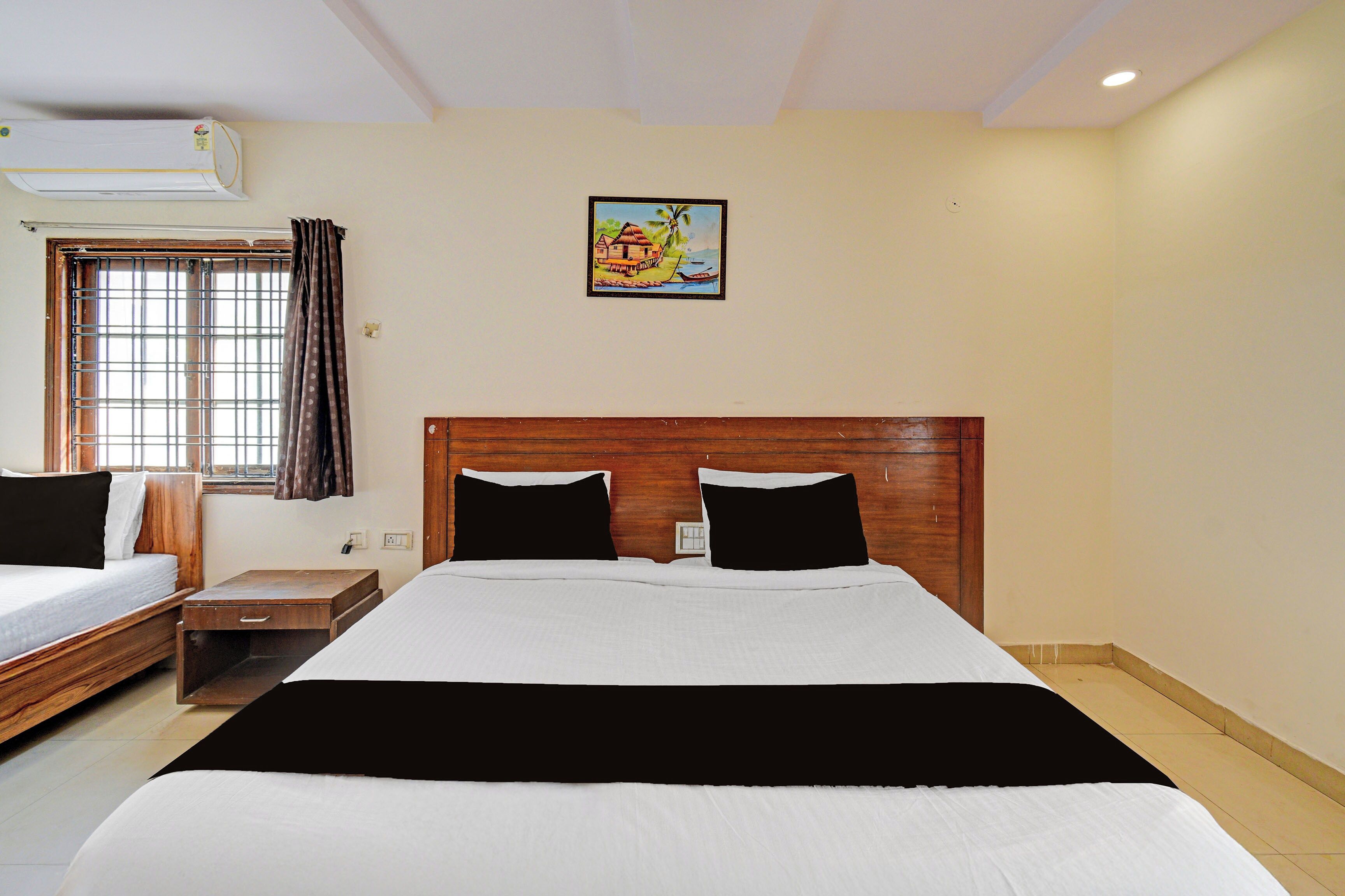 Une chambre d’hôtel avec un grand lit, une table de chevet, une commode, une fenêtre avec des rideaux et un climatiseur fixé au mur.