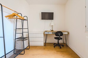 Une chambre équipée d’un bureau, d’une chaise, d’un téléviseur et d’un portant à vêtements avec des cintres.