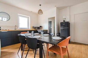 Une cuisine moderne avec une table à manger pour quatre personnes, un réfrigérateur noir et une fenêtre laissant entrer la lumière naturelle.