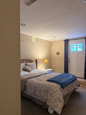 A bedroom with a bed, bedside tables, a lamp, a door, and a window. - Delightful 1-bedroom guesthouse in basement with private entry and free parking (Ellicott City)