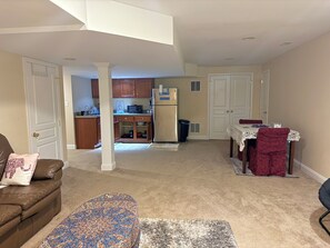 A living room with a brown leather sofa, a patterned ottoman, and a dining area with a table and chairs. - Delightful 1-bedroom guesthouse in basement with private entry and free parking (Ellicott City)
