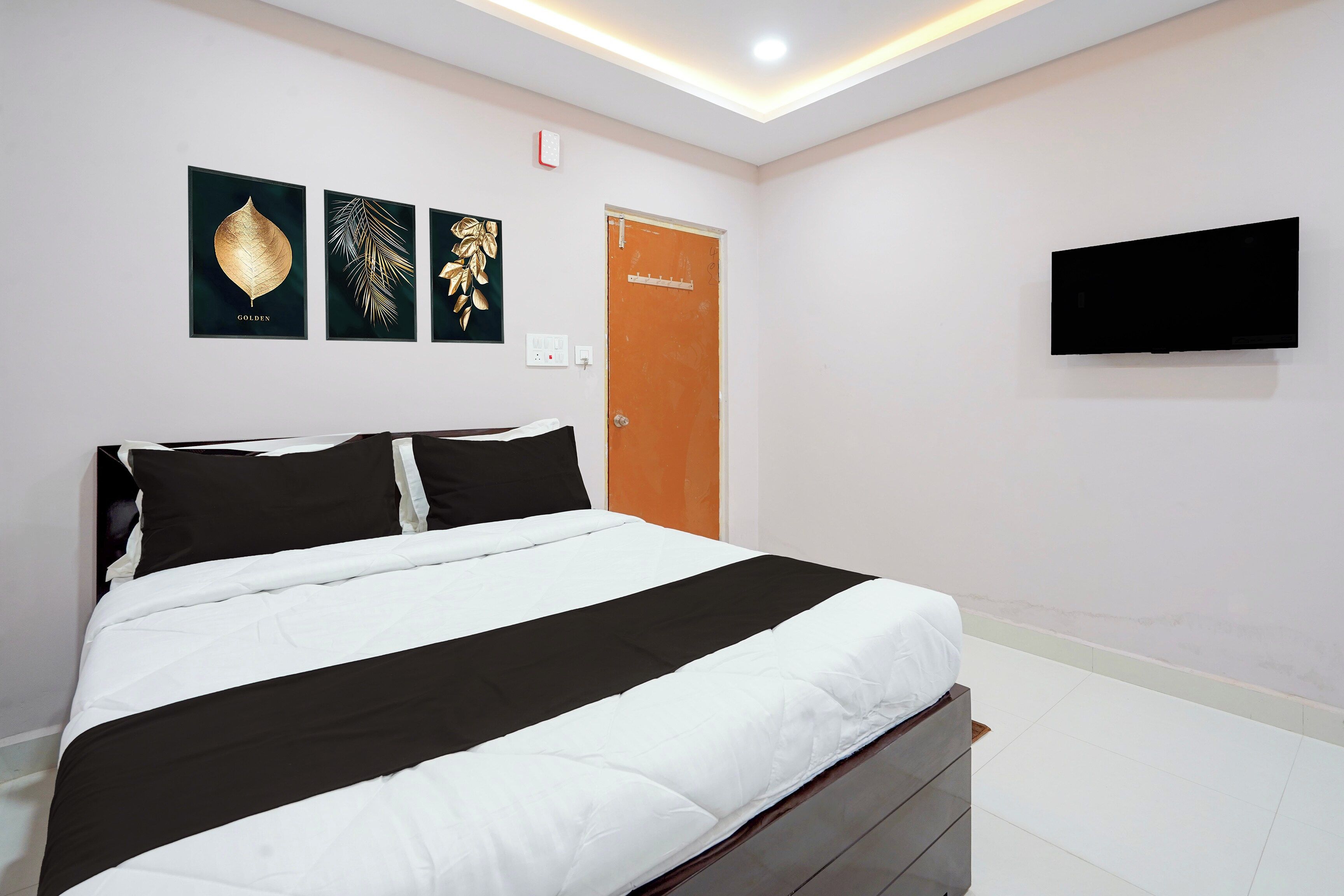 A bedroom with a bed, a flat-screen TV, and three framed wall art pieces.