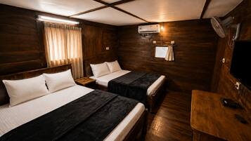 A room with two beds, a wooden floor, a ceiling fan, and a television.