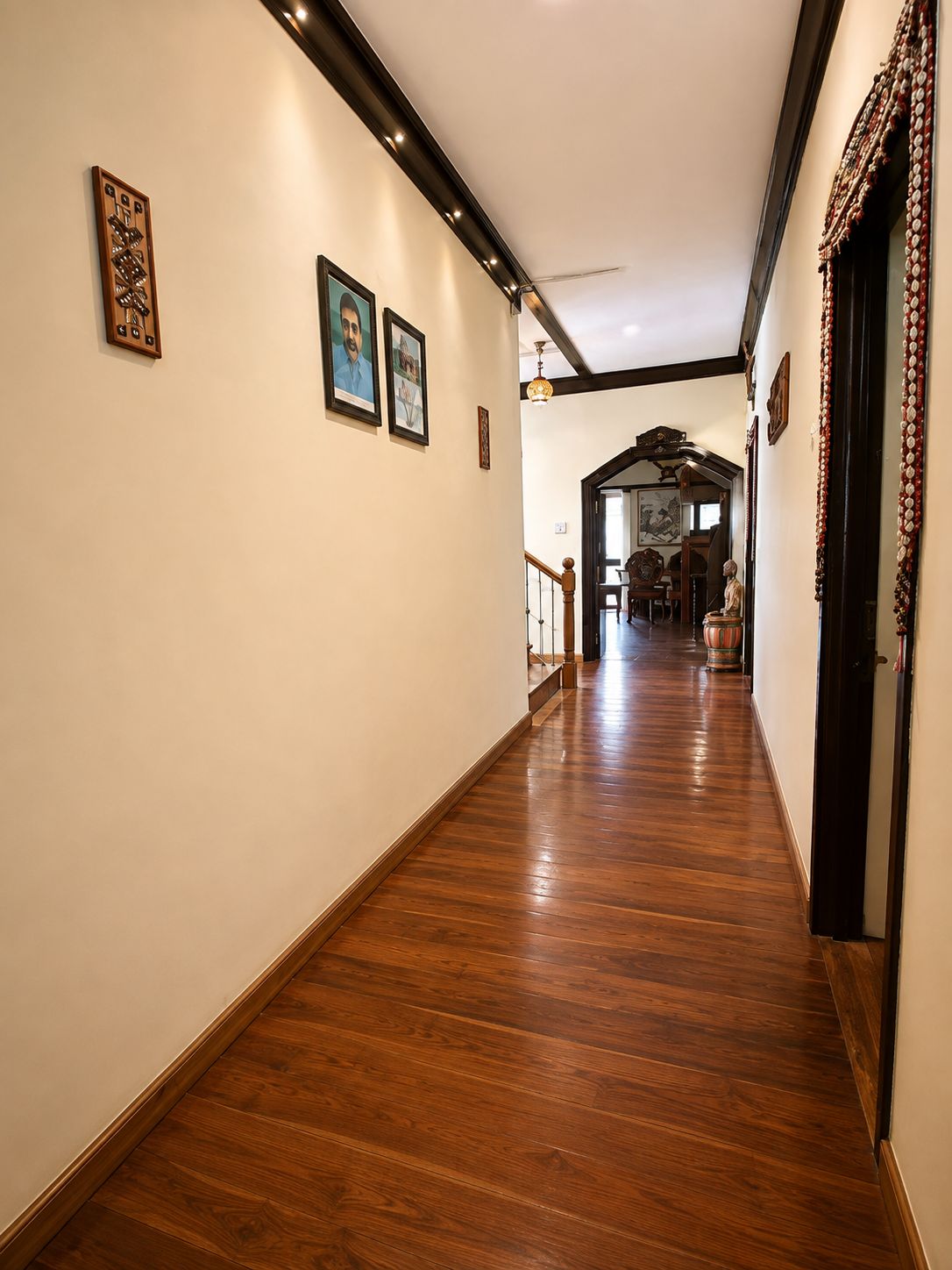 A hallway with wooden flooring, framed pictures on the walls, and a staircase leading to another room.