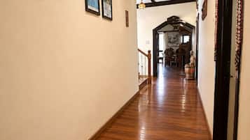 A hallway with wooden flooring, framed pictures on the walls, and a staircase leading to another room.
