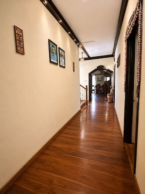A hallway with wooden flooring, framed pictures on the walls, and a staircase leading to another room. - Hotel R.J. House (Abu Road)