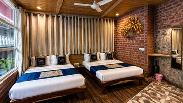A hotel room with two beds, wooden flooring, a brick accent wall, a ceiling fan, and a window with curtains.