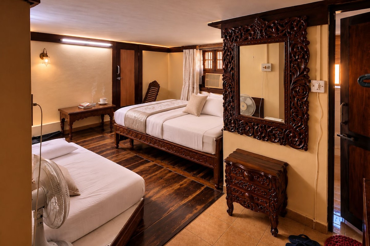 A hotel room with two beds, a wooden dresser, a mirror, and a fan.