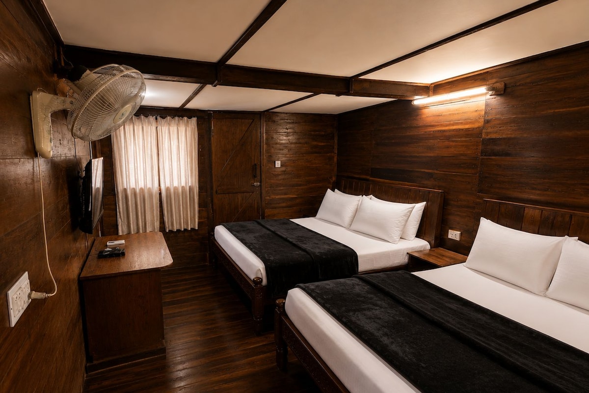 A room with two beds, a desk, a fan, and a television.