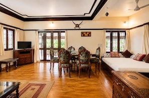 A hotel room with a wooden floor, a bed, a TV, a dining table with chairs, and a ceiling fan. - Hotel R.J. House (Abu Road)