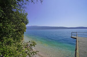 A clear view of a lake with a rocky shoreline and a metal railing overlooking the water.