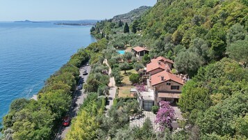 A coastal property with a swimming pool, multiple buildings, and a road alongside the sea.