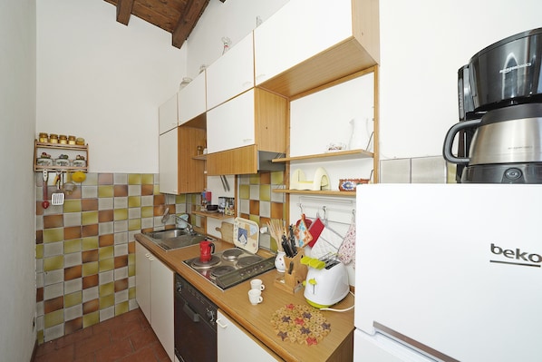 A compact kitchen with wooden cabinets, a tiled backsplash, and a coffee maker. - Appartamento Bouganville (Toscolano Maderno)