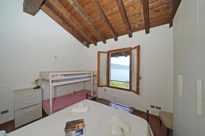 A bedroom with a bunk bed, a desk with a lamp, a window with a view, and a chair. - Appartamento Bouganville (Toscolano Maderno)