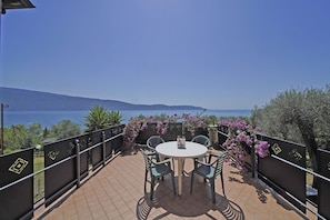 A terrace with a round table and chairs, overlooking a body of water and hills. - Appartamento Bouganville (Toscolano Maderno)