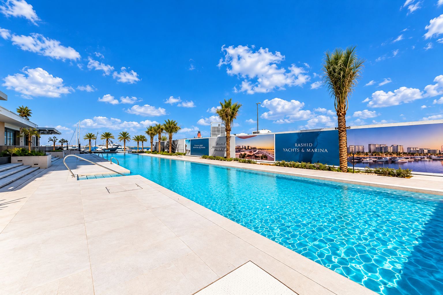 A swimming pool with clear blue water, surrounded by palm trees and a modern building with a sign for Rashid Yachts & Marina.
