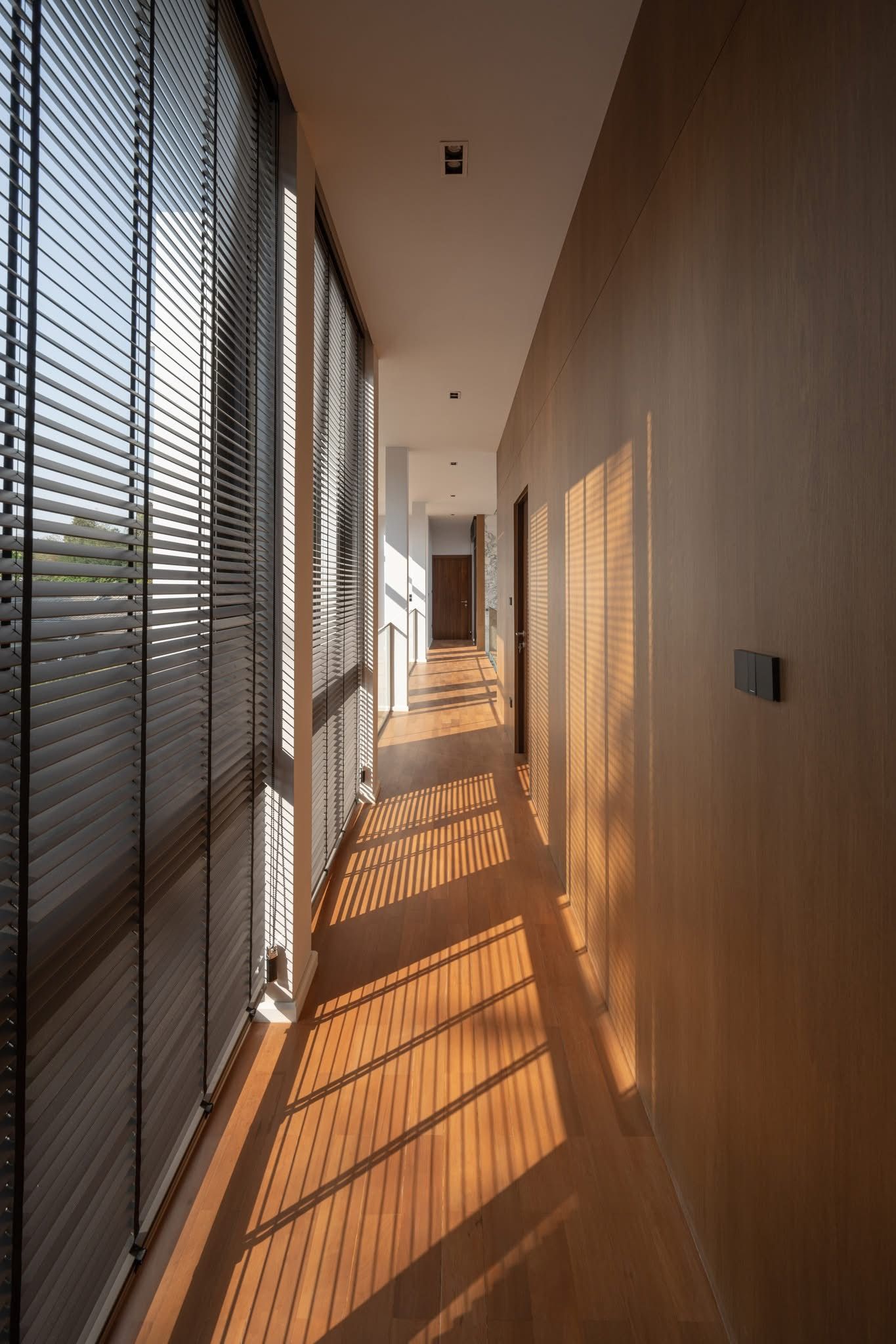 A corridor with horizontal blinds, a wooden floor, and a light-colored wall.