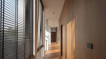 A corridor with horizontal blinds, a wooden floor, and a light-colored wall.