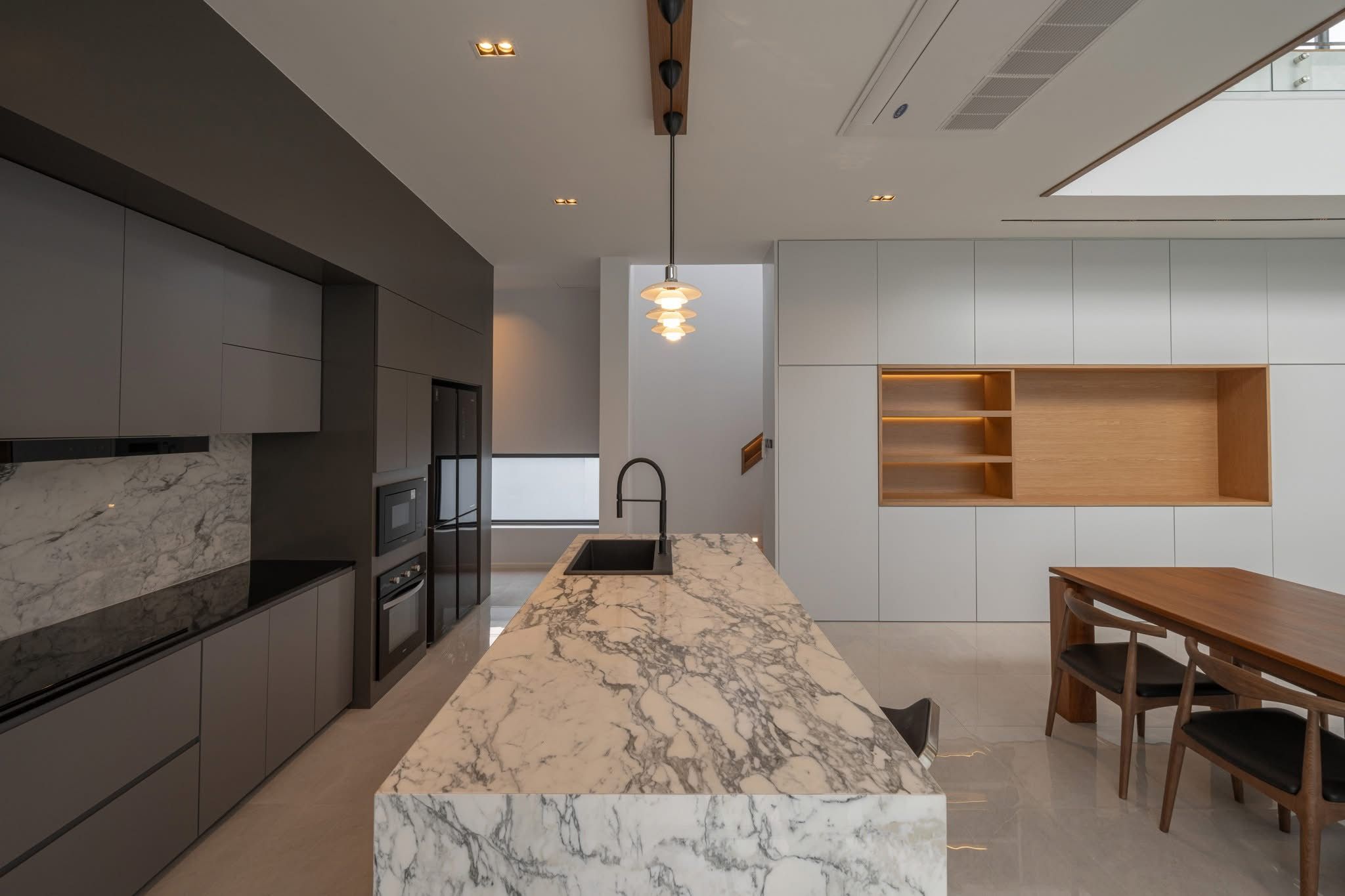 A modern kitchen with a marble island, dark cabinetry, and a wooden dining table.