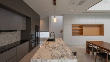 A modern kitchen with a marble island, dark cabinetry, and a wooden dining table.