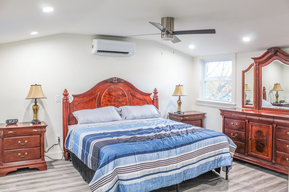 Ein Schlafzimmer mit einem großen Bett, zwei Nachttischen, einem Deckenventilator, einer Klimaanlage, einem Fenster und einem Spiegel.