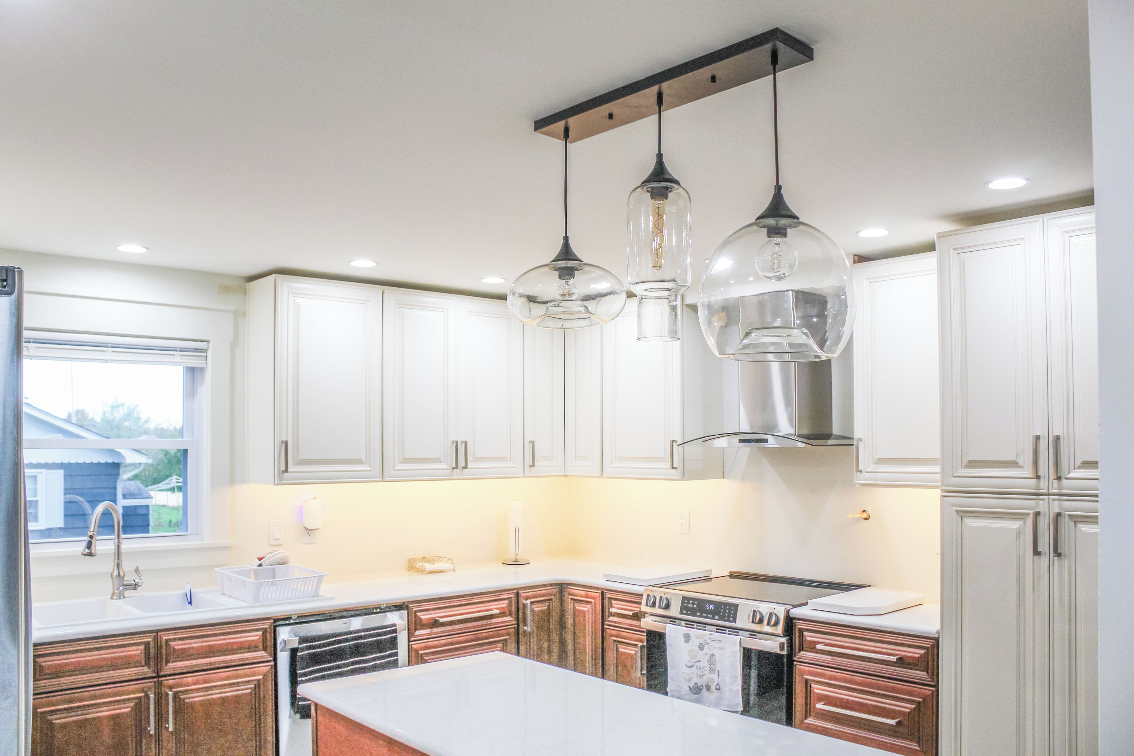 Una cocina moderna con armarios blancos, una campana extractora de acero inoxidable e iluminación colgante.