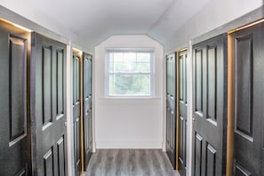 A hallway with dark wooden doors, a white wall, and a window at the end. - Depot - Newly Renovated 3BR Home (Waldoboro)
