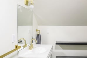 Ein Badezimmer mit einem weißen Waschbecken, goldenen Armaturen, einem großen Spiegel und einem Handtuchhalter.
