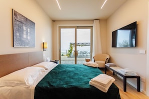 Ett hotellrum med en säng, en stol, ett bord, en tv och utsikt över omgivningarna.