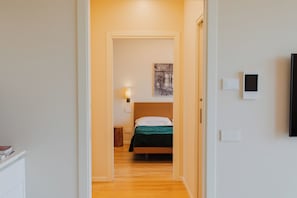 Een hotelkamer met een houten vloer, een bed met een deken in groen en zwart, een wit kussen en een wandlamp.
