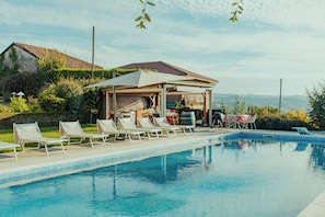En pool med solstolar, en möblerad sittgrupp under tak och utsikt över det omgivande landskapet.