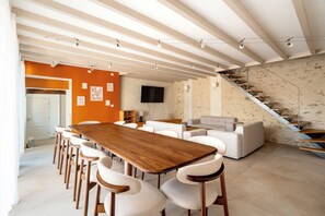Un intérieur moderne avec une table à manger en bois, des chaises blanches, un canapé et un escalier.