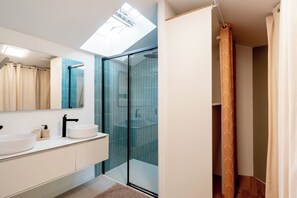 Une salle de bain moderne dotée d’une lucarne, d’une cabine de douche en verre et d’un grand miroir.