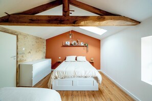 Une chambre avec un plafond en pente, un lit, une commode et une étagère murale agrémentée d’objets décoratifs.