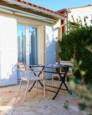 Eine Terrasse im Freien mit Tisch und Stühlen, einer weißen Tür und einem grünen Busch.