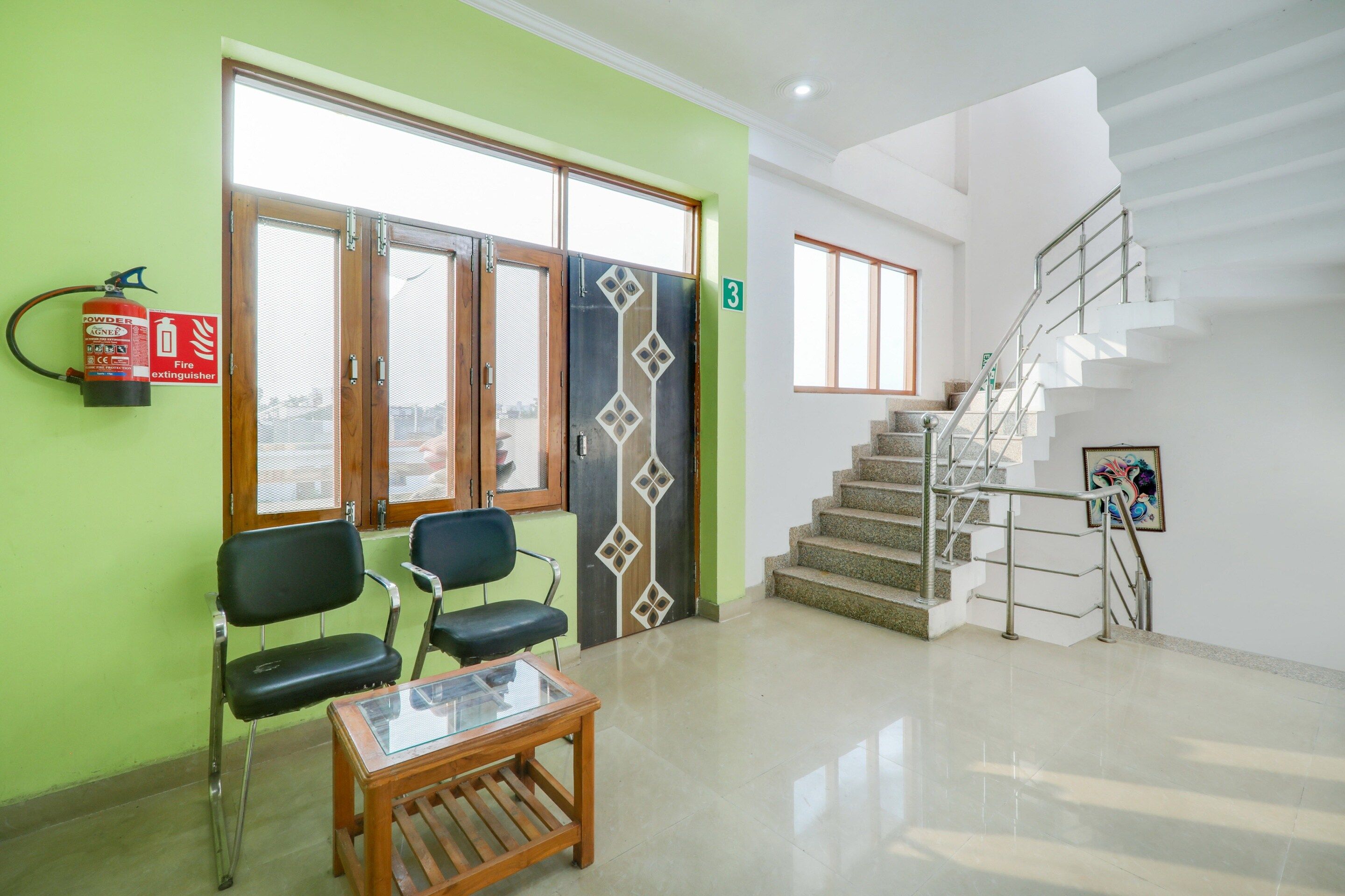 A reception area with a fire extinguisher, two chairs, a glass-top table, and a staircase.