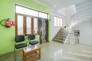 A reception area with a fire extinguisher, two chairs, a glass-top table, and a staircase. - Hotel O Elite Stay Inn (Lucknow)