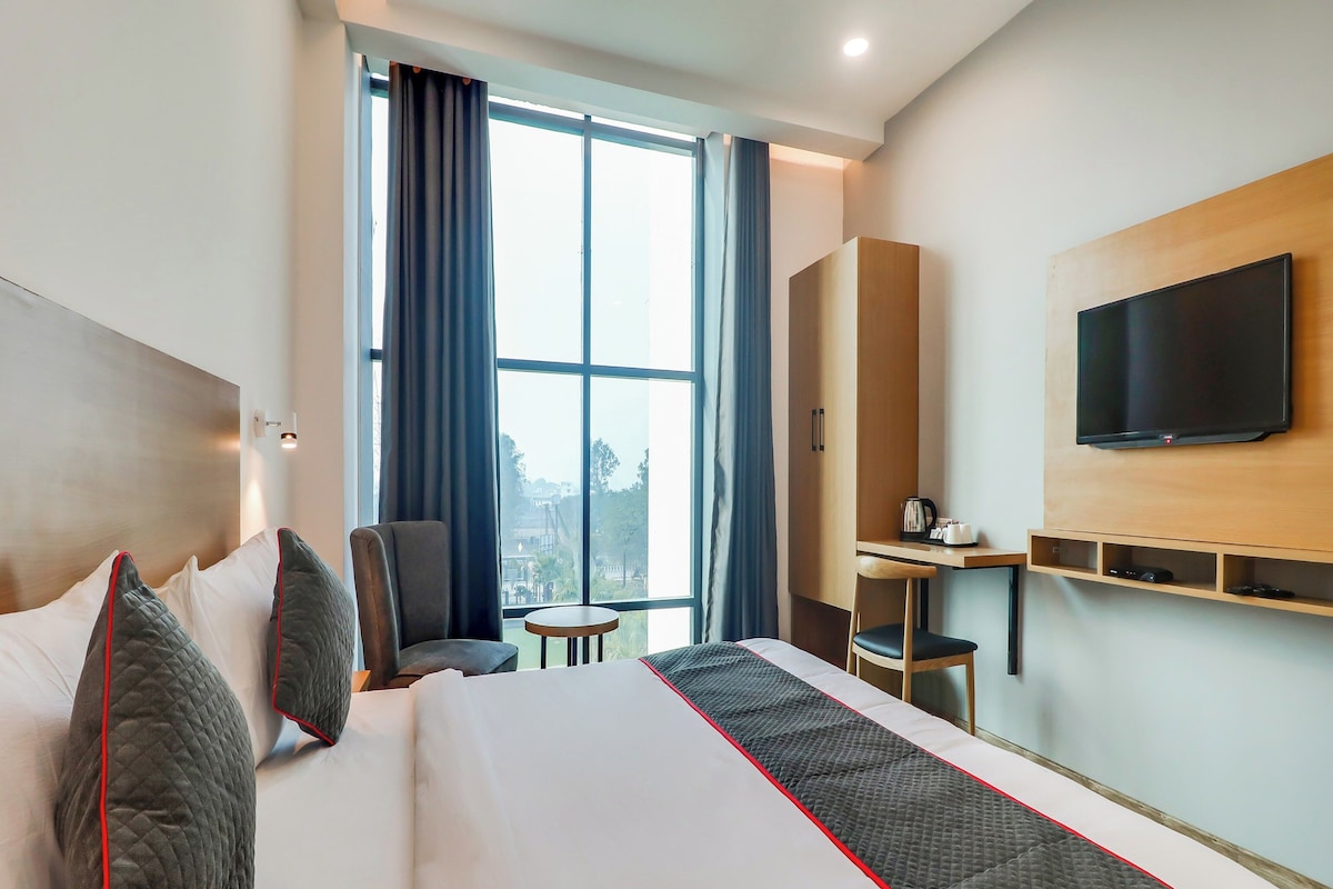 A hotel room with a large bed, a desk, a chair, a TV, and a view of the outdoors.