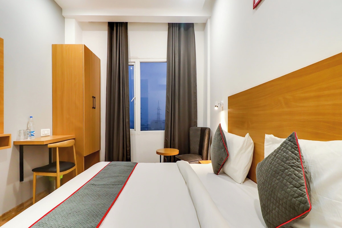 A hotel room with a bed, a desk, a chair, a small table, and a window with curtains.