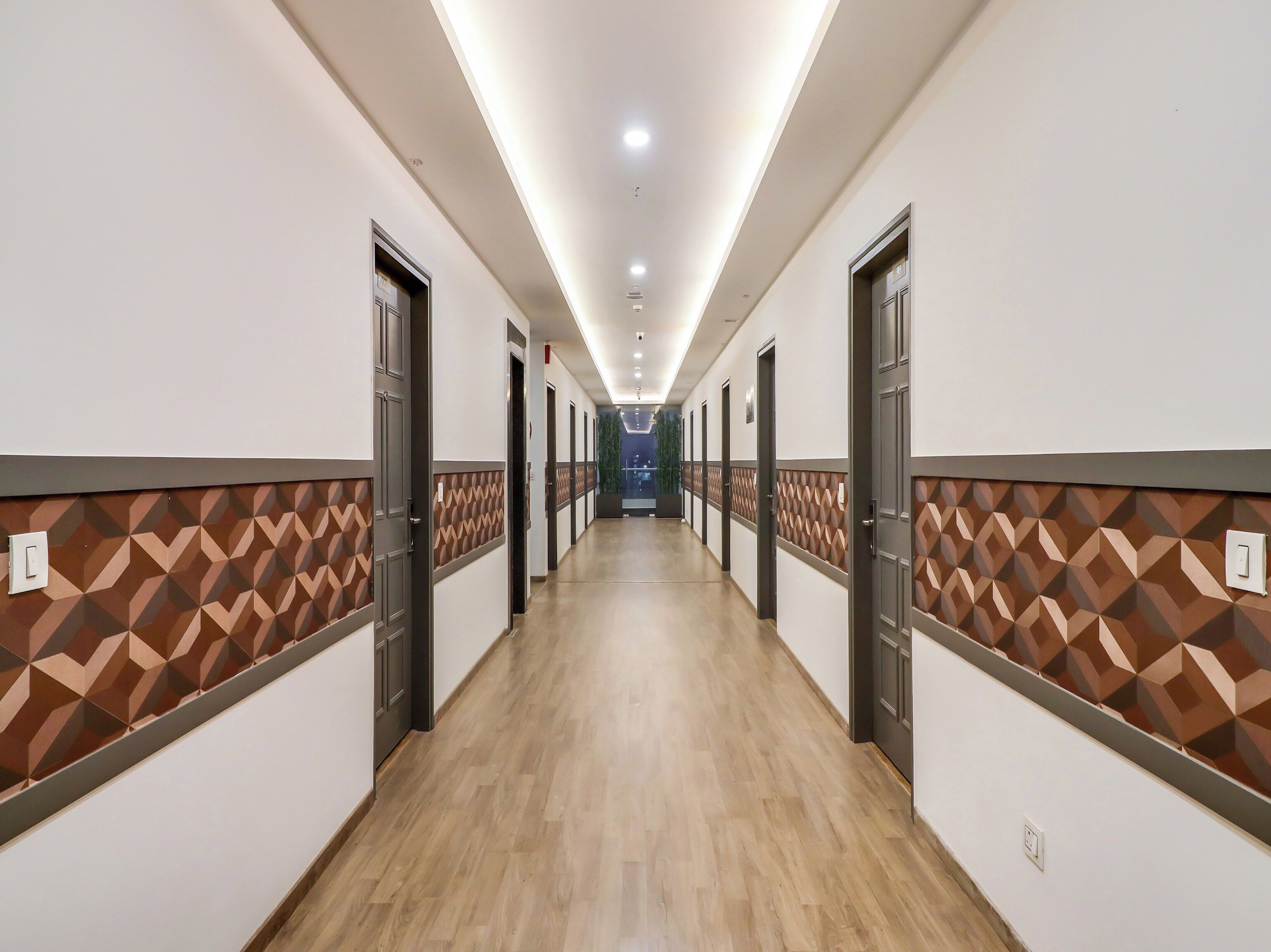 Un pasillo de hotel con puertas a ambos lados, un diseño de pared estampado y suelo de madera.