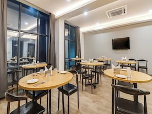 A conference room with multiple tables and chairs, large windows, and a flat-screen TV on the wall. - Townhouse Jashn (Lucknow)