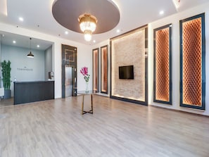 A modern reception area with a reception desk, a mounted TV, and a decorative vase with flowers. - Townhouse Jashn (Lucknow)