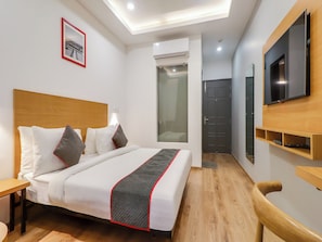 A hotel room with a bed, a TV, a wooden headboard, a bedside table, a wall-mounted shelf, and a door. - Townhouse Jashn (Lucknow)